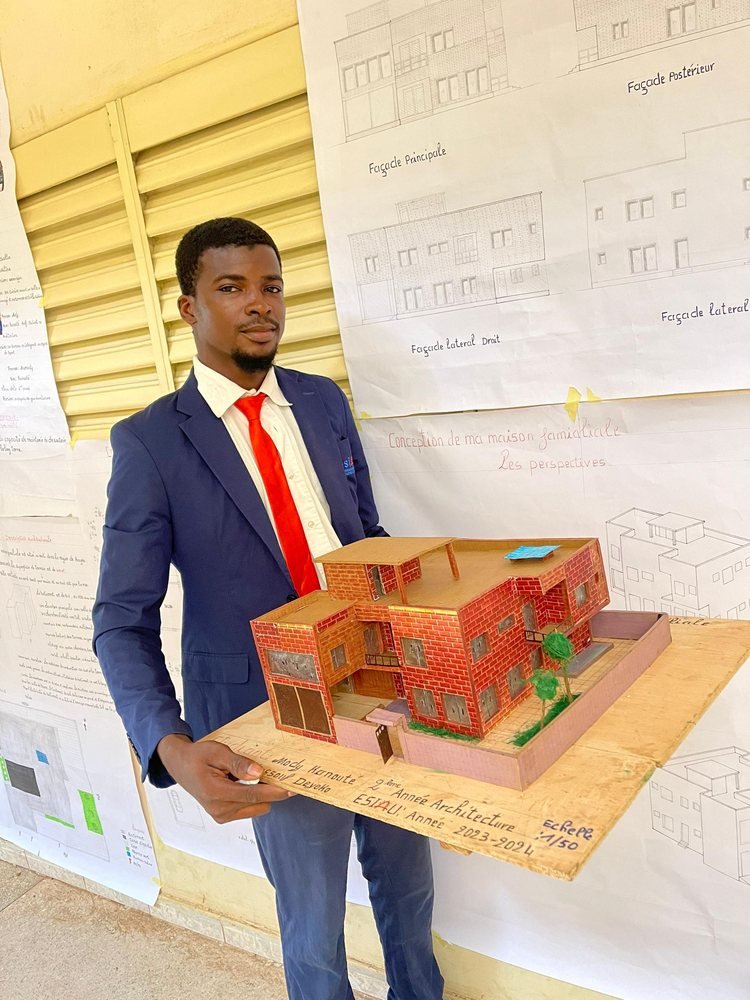 Un étudiant en costume tient une maquette en briques rouges