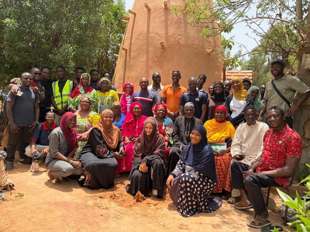 Un groupe d'étudiants et de visiteurs pose devant une tour en terre crue