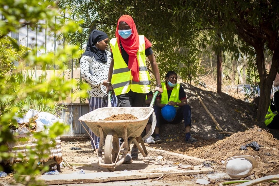 Une étudiante pousse une brouette de terre sur un chantier-école