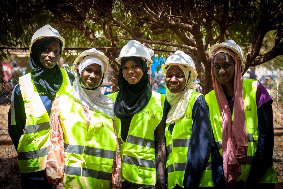 Quatre étudiantes en casque et gilet de sécurité sourient à l'objectif