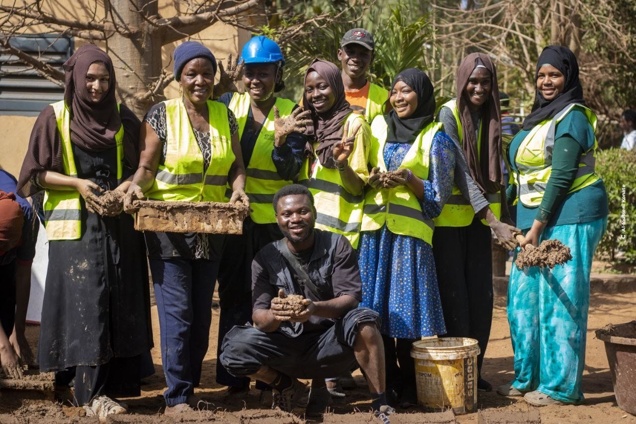 Un groupe d'étudiants en gilet de sécurité sourit autour d'un atelier de construction en terre